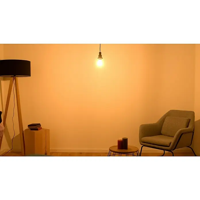 Osram LED-Lampen Set Glühlampenform E27 klar - E27, Nicht Dimmbar, Warmweiß, 1.521 lm, 11 W, Klar - Ein gemütliches Wohnzimmer mit einem grauen Sessel, einem kleinen Tisch mit Kerzen und einer Stehlampe, beleuchtet durch eine hängende Glühbirne.