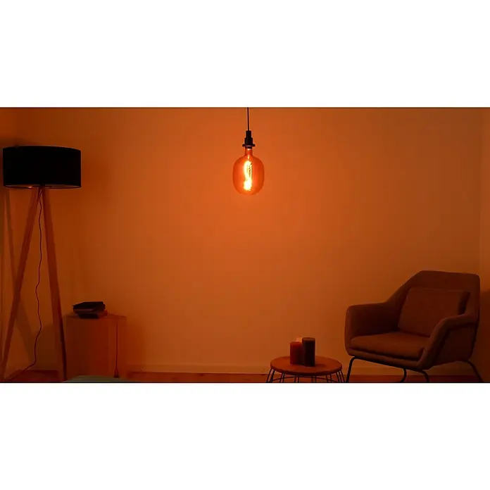 Osram LED-Lampe Vintage Edition 1906 Globe-Form E27 - E27, Dimmbar, Warmweiß, 220 lm, 4,5 W, Farbe: Pink - Warmes Interieur mit einer einzelnen Glühbirne, Stehlampe und Sessel, die eine gemütliche und entspannende Atmosphäre schaffen.