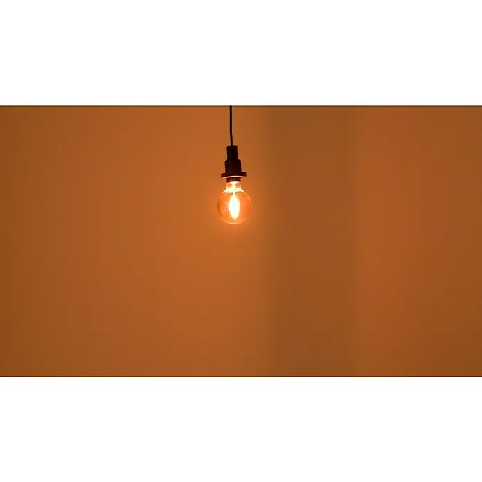 Osram LED-Lampe Vintage Edition 1906 Globe-Form E27 - E27, Nicht Dimmbar, Warmweiß, 100 lm - Eine glühende Edison-Glühbirne hängt an einem schwarzen Kabel vor einem warmen, orangefarbenen Hintergrund und verbreitet ein sanftes, atmosphärisches Licht.
