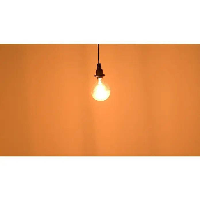 Osram LED-Lampe Vintage Edition 1906 Globe-Form E27 - E27, Dimmbar, Warmweiß, 470 lm, 5,8 W - Glühbirne an einer Schnur mit warmem Licht vor orangefarbenem Hintergrund.