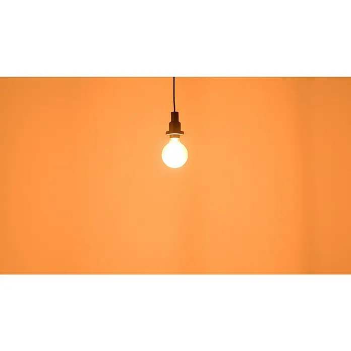 Osram LED-Lampe Vintage Edition 1906 Globe-Form E27 - Durchmesser: 9,5 cm, E27, Dimmbar, Warmweiß, 806 lm, 8,8 W - Glühbirne mit warmem Licht an einer schwarzen Fassung und einem schwarzen Kabel vor orangefarbenem Hintergrund.