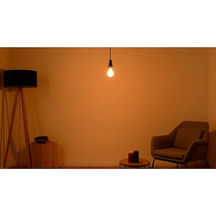 Osram LED-Lampe Vintage Edition 1906 Globe-Form E27 - Durchmesser: 9,5 cm, E27, Dimmbar, Warmweiß, 420 lm, 4,8 W - Gemütliches Wohnzimmer mit Stehlampe, Sessel und hängender Glühbirne, alles in warmen Farben. Eine behagliche Atmosphäre zum Entspannen.