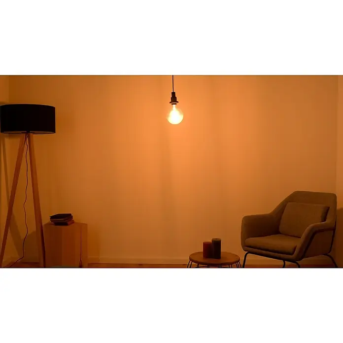 Osram LED-Lampe Vintage Edition 1906 Globe-Form E27 - E27, Dimmbar, Warmweiß, 470 lm, 5,8 W - Innenraum mit Stehlampe, Hängelampe, Sessel und Tisch mit Kerzen. Warmes Licht schafft eine gemütliche Atmosphäre.