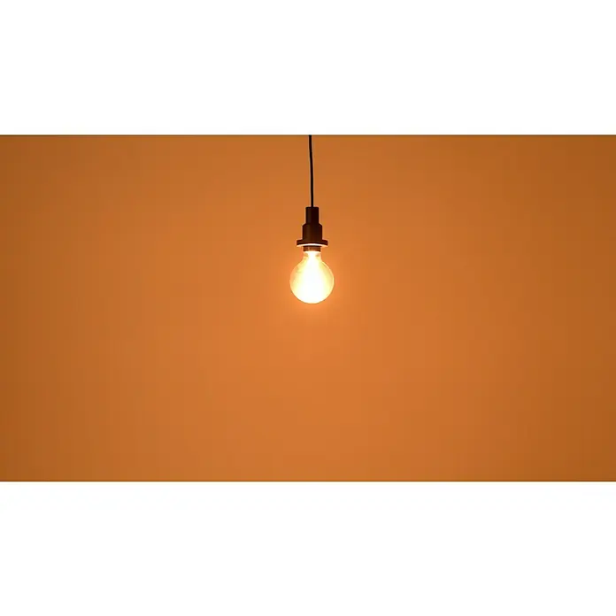 Osram LED-Lampe Vintage Edition 1906 Globe-Form E27 - Durchmesser: 9,5 cm, E27, Dimmbar, Warmweiß, 420 lm, 4,8 W - Helle Vintage-Glühbirne, die warmes Licht ausstrahlt, hängt an einem schwarzen Kabel vor einem orangefarbenen Hintergrund.
