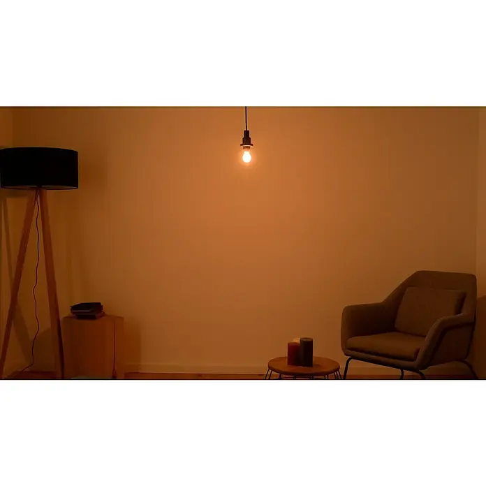 Osram LED-Lampe Vintage Edition 1906 Birnenform E14 - E14, Dimmbar, Warmweiß, 250 lm, 34 W - Gemütliches Wohnzimmer mit Stehlampe, Sessel und Kerzen. Die gedämpfte Beleuchtung schafft eine entspannende Atmosphäre im Raum.