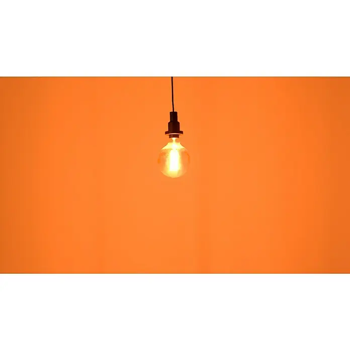 Osram LED-Lampe Vintage Edition 1906 Globe-Form 125 E27 - E27, Dimmbar, Warmweiß, 500 lm, 11 W - Nahaufnahme einer klaren Glühbirne mit Edison-Glühfaden, die von einer schwarzen Fassung an einer Schnur unter einem warmen, orangefarbenen Hintergrund hängt.
