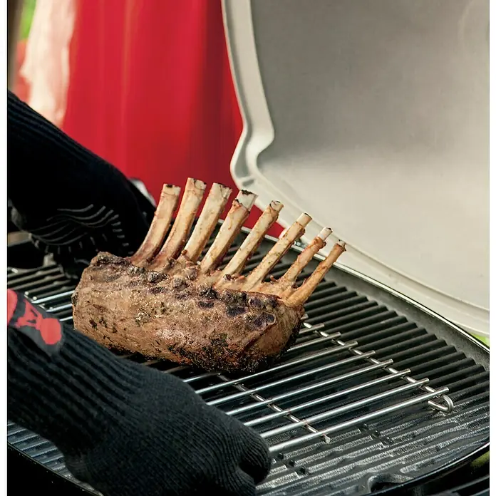 Weber Grillrost - Passend für: Weber Q 2000 Serie - Ein saftiger Lammkarree wird auf einem Grill zubereitet, wobei schwarze Grillhandschuhe die Zubereitung erleichtern.