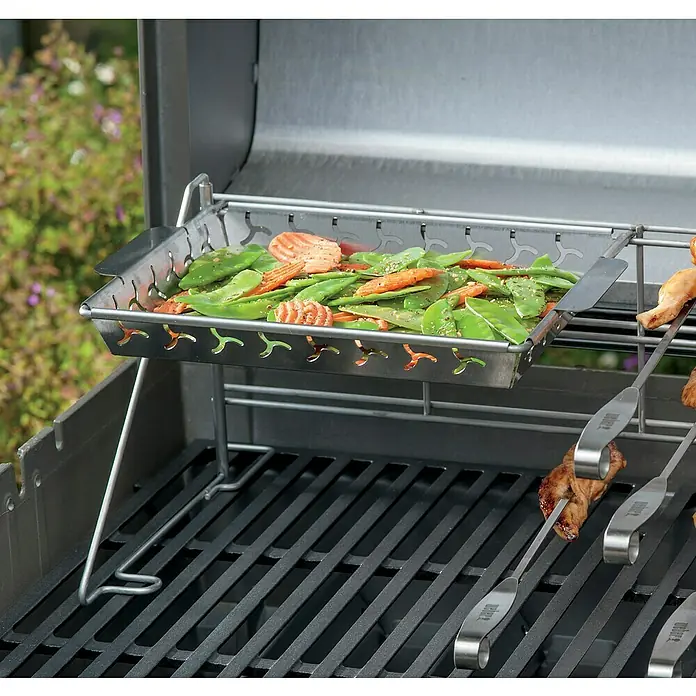 Weber Grillkorb - Edelstahl - Der Weber Grillkorb ist mit Gemüse gefüllt und wird auf einem Grill mit Fleischspießen zubereitet. Er ermöglicht das Grillen kleiner Speisen.
