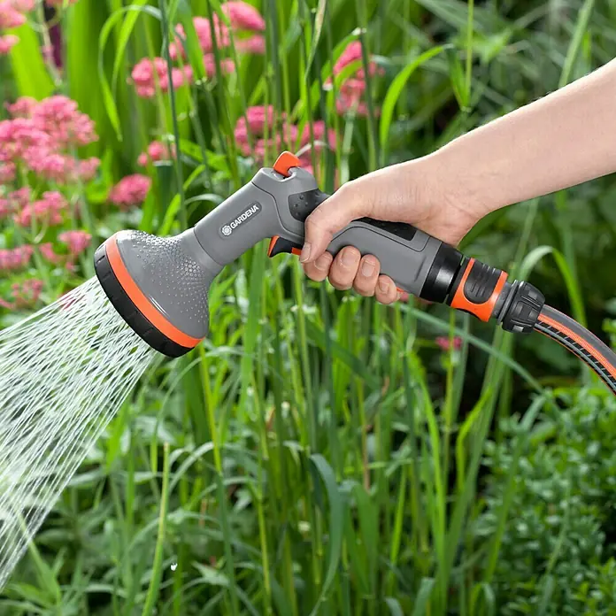 Gardena Comfort Brause - Anzahl Sprühformen: 2 Stk., Metall/Kunststoff, Geeignet für: Pflanzreihenbewässerung - Nahaufnahme einer Hand, die eine Gardena-Gartenspritze hält, die Wasser auf Blumen und Pflanzen in einem Garten sprüht.