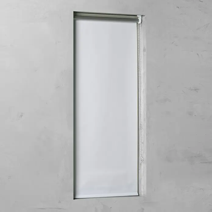 Rollo Basic - B x H: 60 x 175 cm, Weiß, Uni, Verdunkelnd - Eine heruntergelassene, weiße Jalousie vor einer grauen Betonwand. Der Rollomechanismus ist sichtbar und akzentuiert das minimalistische Design.