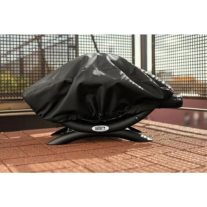 Weber Funda protectora para barbacoa Q1000 - Específico para: Weber serie Q 100, Plástico - Parrilla Weber cubierta en un patio. La funda negra protege la parrilla del clima y la mantiene limpia y lista para usar.