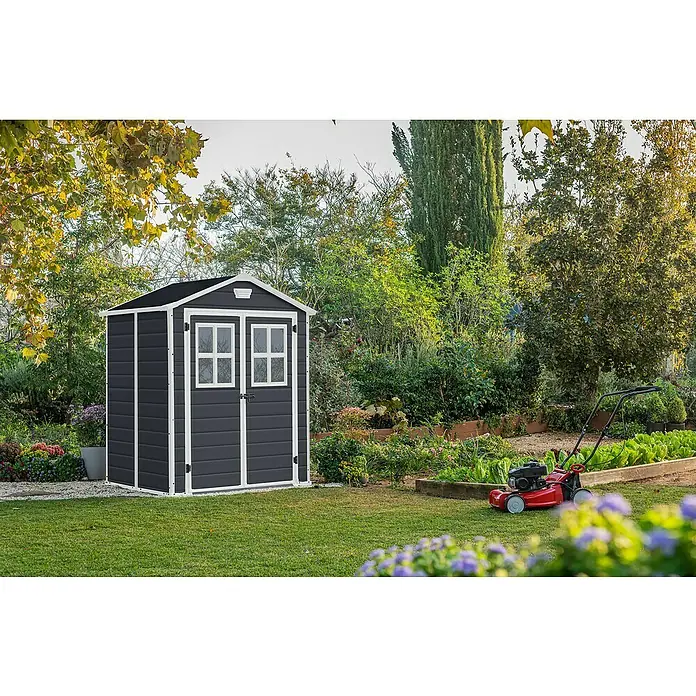 Keter Gerätehaus Manor 6x5 - Außenmaß inkl. Dachüberstand (B x T): 185 x 152 cm, Kunststoff, Anthrazit/Weiß - Ein graues Gartenhaus mit weißen Akzenten und einem schwarzen Dach vor einem Garten mit Rasenmäher.