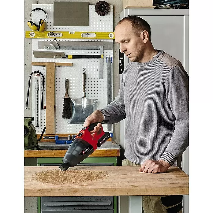 Einhell Power X-Change 18V Akku-Handstaubsauger TE-VC 18 Li-Solo - 18 V, Ohne Akku - Ein Mann nutzt einen rot-schwarzen Einhell Akku-Handstaubsauger, um Holzspäne von einer Werkbank zu entfernen.