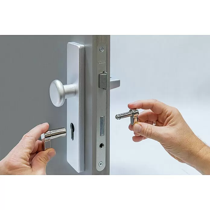 Abus Blindzylinder BlindFlex N L B/D - Vernickelt - Hände montieren ein silberfarbenes Türgriff-Set mit rundem Knopf und Hebel an einer grauen Tür.