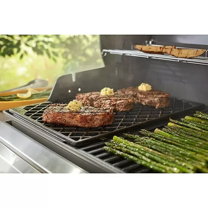 Weber Grilleinsatz Sear-Grate - Passend für: Weber Gasgrills Genesis II - Steaks mit schmelzender Butter und Spargel braten auf schwarzen Grillrosten, mit Essen auf einem Warmhalterost im Freien.
