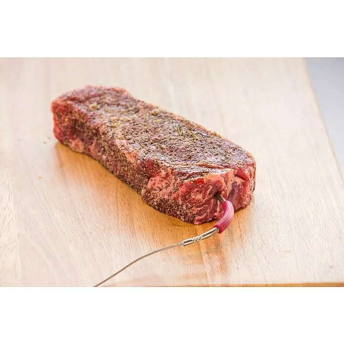 Weber Ersatz-Messfühler iGrill Pro - Passend für: Weber Thermometer iGrill, Kerntemperaturmessung - Nahaufnahme eines rohen, gewürzten Rindersteaks mit einem Thermometer, das in ein Holzbrett gesteckt ist. Ideal zum Grillen oder Braten.