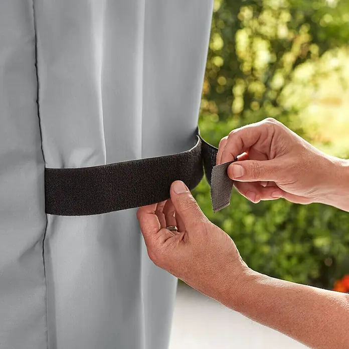 Weber Standard Grill-Schutzhülle - Passend für: Weber Genesis II 200-Serie - Nahaufnahme einer Person, die einen schwarzen Klettverschluss an einer grauen Abdeckung befestigt.
