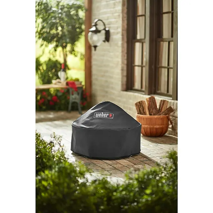 Weber Grill-Schutzhülle Fireplace - Passend für: Weber Feuerstelle Fireplace - Ein Weber-Feuertisch mit einer schwarzen Schutzhülle darauf, der Weber-Schutz vor den Elementen bietet und das Produkt sauber hält.