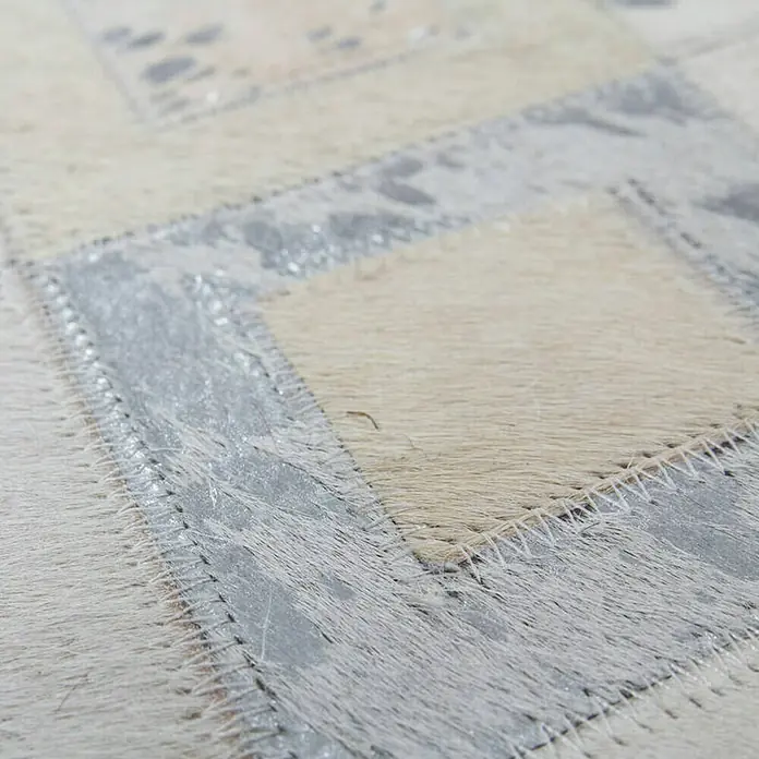 Kayoom Lederteppich Dazzle 100 - Grau/Silber, 230 x 160 cm, 100 % Leder - Detailansicht eines Patchwork-Teppichs mit hellen und silberfarbenen Fellstücken, die durch Zickzacknähte verbunden sind. Die Textur des Fells ist deutlich sichtbar.