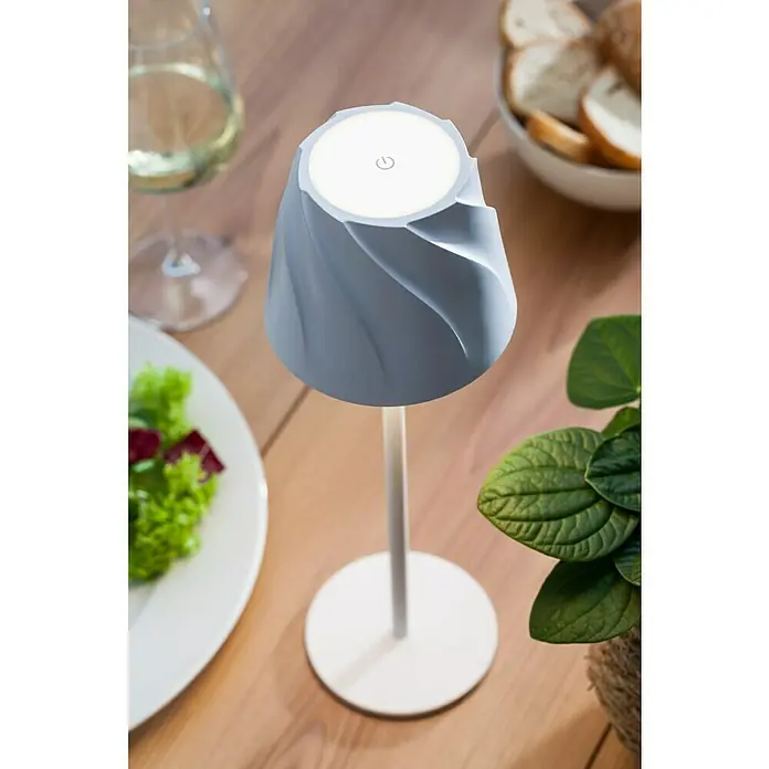 Starlux Akku-Tischleuchte Loreo - 4 W, L x B x H: 11 x 11 x 36 cm, Weiß, Warmweiß - Nahaufnahme einer modernen, spiralförmigen Tischleuchte mit LED-Licht auf einem Holztisch, umgeben von Speisen und Getränken.