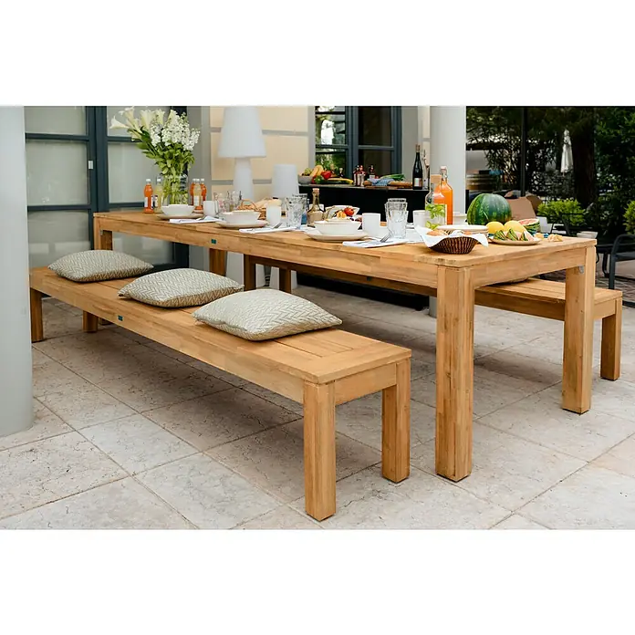 Sunfun Laura Gartentisch - L x B x H: 220 x 100 x 76 cm, Akazie, Rechteckig, Naturbraun - Einladender Außenbereich mit großem Esstisch und Bänken aus Holz, dekoriert mit Kissen und Geschirr für eine Mahlzeit im Freien.