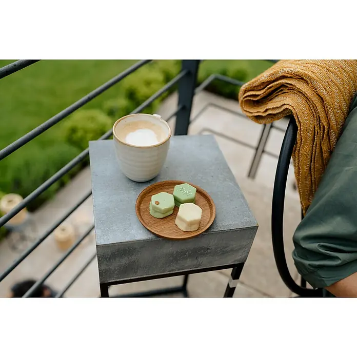 Tasse Tabo - Ø x H: 9 x 9 cm, Weiß, Keramik - Nahaufnahme von Cappuccino und einem Teller mit veganen Pralinen auf einem grauen Tisch, ergänzt durch eine Decke auf einem Stuhl im Hintergrund.