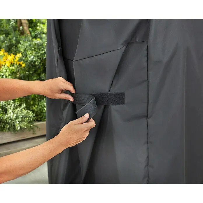 Weber Grill-Schutzhülle - Passend für: Weber Spirit 200/300 Serie - Eine Person sichert eine schwarze Abdeckung mit einem Klettverschluss um ein Produkt im Freien.