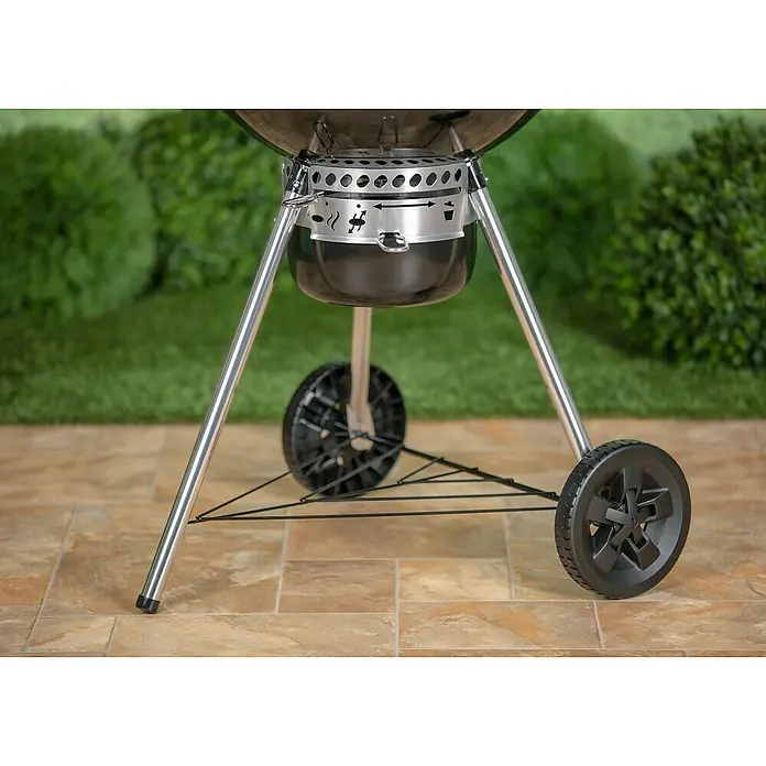 Weber Master-Touch GBS Kugelgrill Premium E-5770 - Durchmesser Grillfläche: 57 cm, Schwarz/Silber - Nahaufnahme eines Holzkohlegrills mit silbernen Beinen und schwarzen Rädern vor einem grünen Hintergrund.
