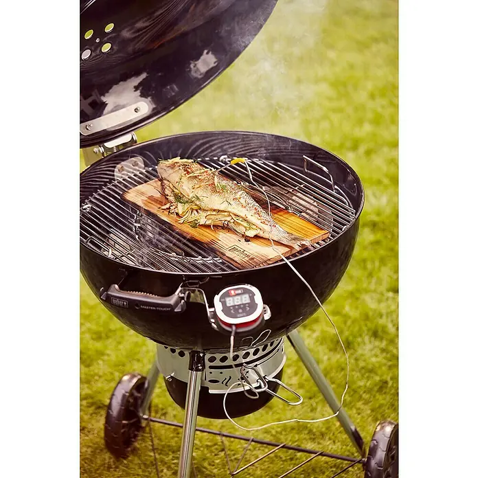Weber Master-Touch GBS Kugelgrill Premium E-5770 - Durchmesser Grillfläche: 57 cm, Schwarz/Silber - Gegrillter Fisch auf Zedernholzbrett in einem Weber Holzkohlegrill. Das Essen wird mit einem digitalen Thermometer überwacht.