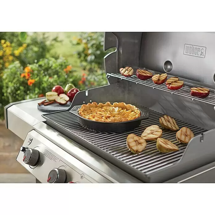 Weber Backform - Keramik - Edelstahl-Gasgrill von Weber backt einen Apfelkuchen und grillt Apfel- und Birnenhälften im Freien.