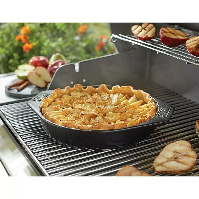 Weber Backform - Keramik - Apfelkuchen in einer schwarzen Backform auf einem Grill, mit gegrillten Apfelhälften.