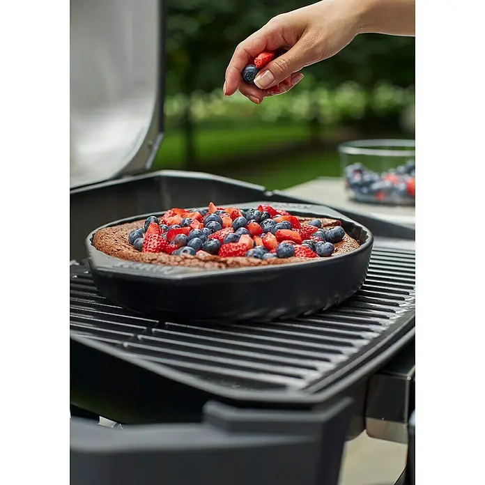 Weber Backform - Keramik - Ein Schokoladenkuchen wird mit frischen Erdbeeren und Blaubeeren auf einem Grill dekoriert. Köstliche Sommerdessert-Idee für Grillpartys.