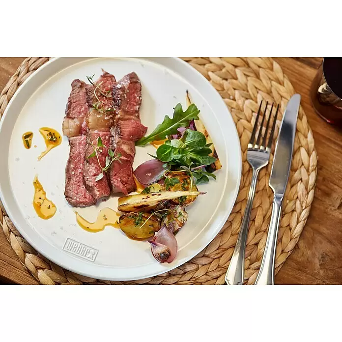Weber Teller - Keramik, Durchmesser: 20 cm - Weißer ovaler Weber-Teller mit Steak, Gemüse und Salat, auf einem geflochtenen Untersetzer angerichtet.