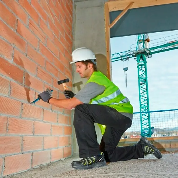 Bellota Maza 53080 - Largo: 39 mm, 1.000 g - Un trabajador de la construcción con casco y chaleco trabaja en una pared de ladrillo con un martillo y un cincel.