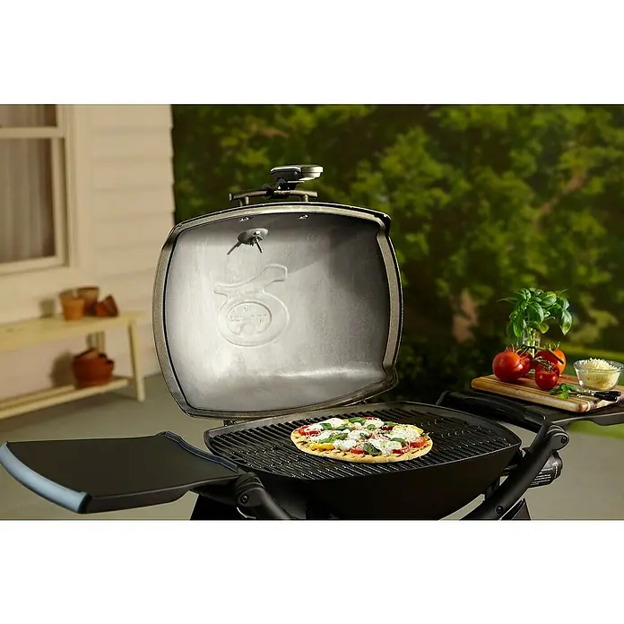 Weber Grifflicht Q - Passend für: Weber Q-Serie - Nahaufnahme eines Weber Grills mit offener Haube, auf dem eine Pizza zubereitet wird. Im Hintergrund Zutaten wie Tomaten und Basilikum.