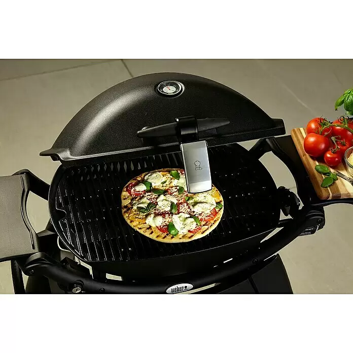 Weber Grifflicht Q - Passend für: Weber Q-Serie - Schwarzer Weber Gasgrill mit einer Pizza auf dem Rost, daneben frische Tomaten und Basilikum.