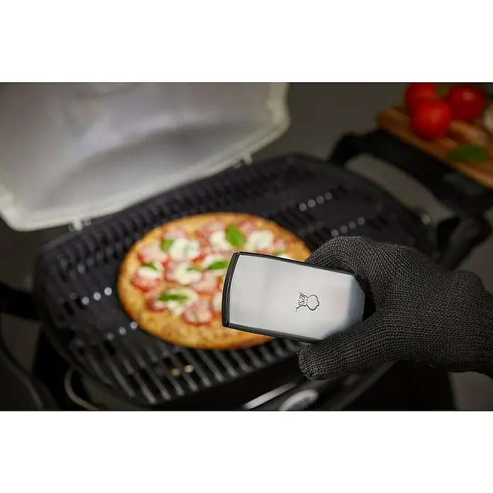 Weber Grifflicht Q - Passend für: Weber Q-Serie - Eine köstliche Pizza wird auf einem Grill zubereitet, mit einem Grillwender in der Hand eines Kochs.