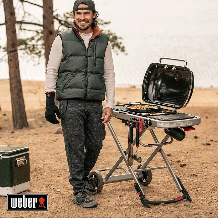 Weber Gasgrill Traveler - Grillfläche (B x T): 63 x 34 cm, 3,8 kW, Anzahl Brenner: 1, Schwarz/Silber - Weber Grill im Freien mit Mann. Der tragbare Gasgrill bietet hohe Leistung und Komfort für unterwegs.