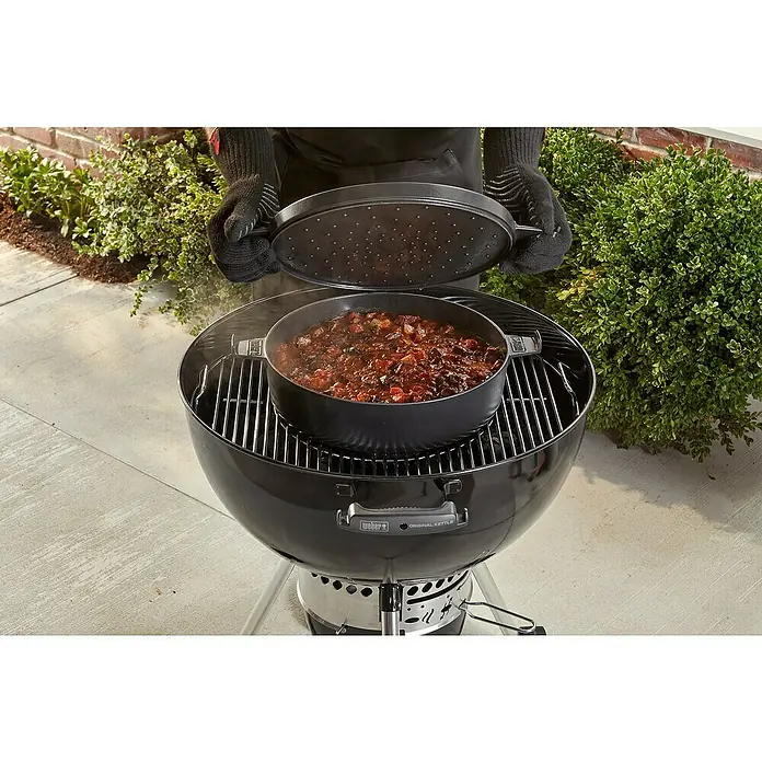 Weber Dutch Oven 2in1 - L x B x H: 33,5 x 42,37 x 12,27 cm, Gusseisen - Ein Weber Kugelgrill mit einem schwarzen Topf auf dem Rost, der mit einem Deckel bedeckt wird. Ideal zum Kochen im Freien.