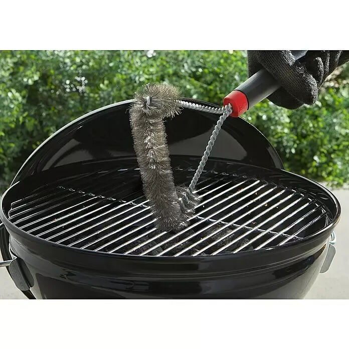 Weber Grillbürste - Länge: 30,5 cm - Eine behandschuhte Hand reinigt mit einer Metall-Grillbürste mit schwarzem und rotem Griff die Roste eines schwarzen Holzkohlegrills.