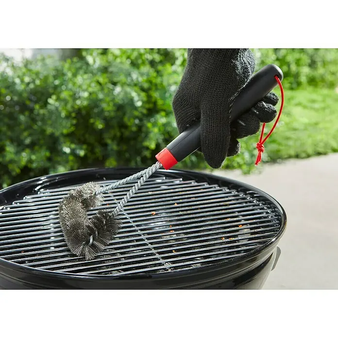 Weber Grillbürste - Länge: 30,5 cm - Eine Person reinigt einen Grillrost mit einer Grillbürste. Die Bürste hat einen schwarzen Griff und rote Akzente.