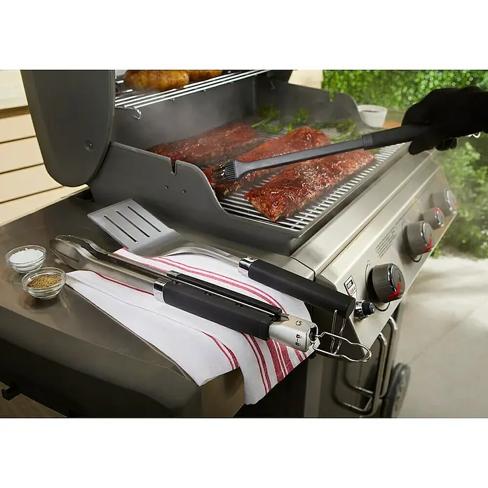 Weber Grillzubehör-Set Precision - Edelstahl - Ein Weber Grill mit Grillwerkzeugen. Auf dem Grillrost liegen Rippchen und Gemüse. Eine Hand pinselt Marinade auf die Rippchen.