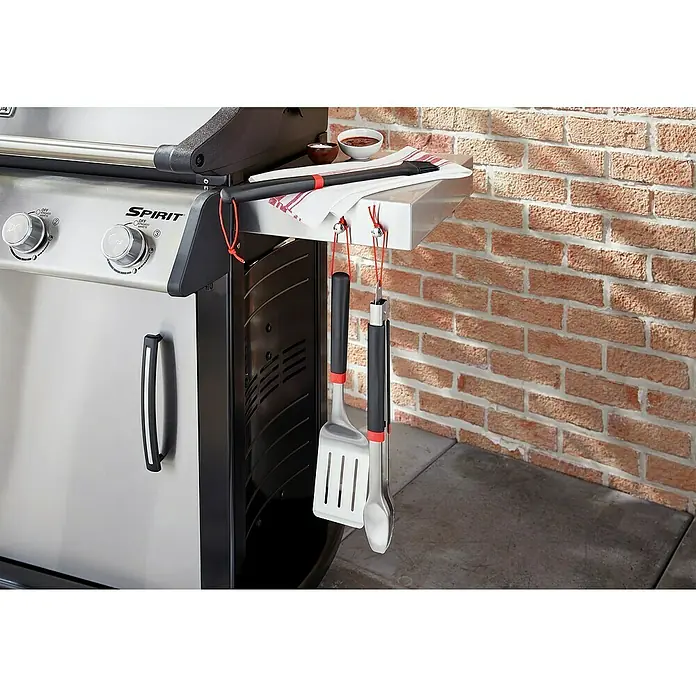 Weber Grillzange - Länge: 40,6 cm - Das Bild zeigt einen Weber Spirit Grill mit Grillwerkzeugen, darunter ein Wender und eine Zange, die an der Seite des Grills hängen.