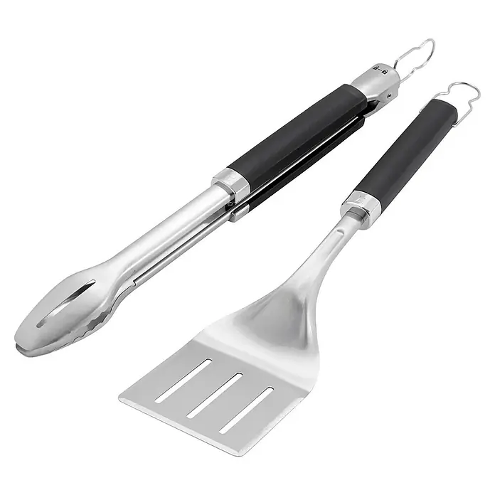 Weber Utensilios para barbacoa Precision - 2 pzs. - Un juego de utensilios para barbacoa que incluye pinzas de acero inoxidable y espátula con mangos negros sobre un fondo negro.