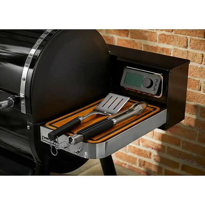 Weber Grillbesteck Set - 2 -tlg. - Detailaufnahme eines Smokefire-Grills mit Grillwerkzeugen auf einem Ablagetisch, der die Marke und Funktionalität hervorhebt.