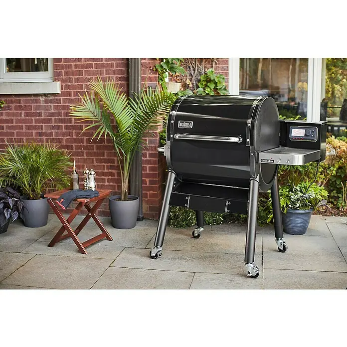 Weber Pelletgrill Smokefire EX4 GBS - Grillfläche (B x T): 61 x 46 cm, Schwarz - Der Weber SmokeFire Grill in Schwarz auf einer Terrasse, umgeben von Pflanzen, bietet die perfekte Möglichkeit für ein BBQ im Freien.