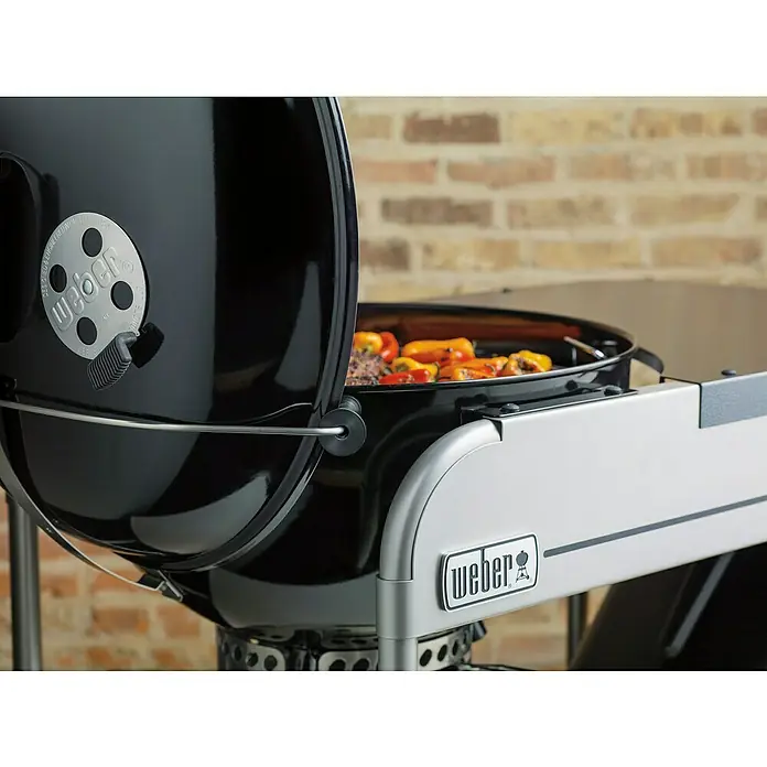 Weber Barbacoa de carbón Performer premium GBS 57 - Diámetro de la superficie de la parrilla: 57 cm, Negro - Primer plano de una barbacoa Weber con la tapa abierta, mostrando comida a la parrilla.