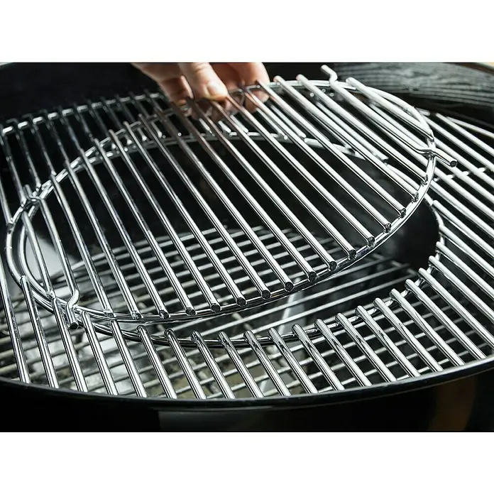 Weber Barbacoa de carbón Performer premium GBS 57 - Diámetro de la superficie de la parrilla: 57 cm, Negro - Primer plano de dos rejillas de parrilla redondas cromadas. Una rejilla es sostenida por una mano, mientras que la otra descansa dentro de la parrilla.