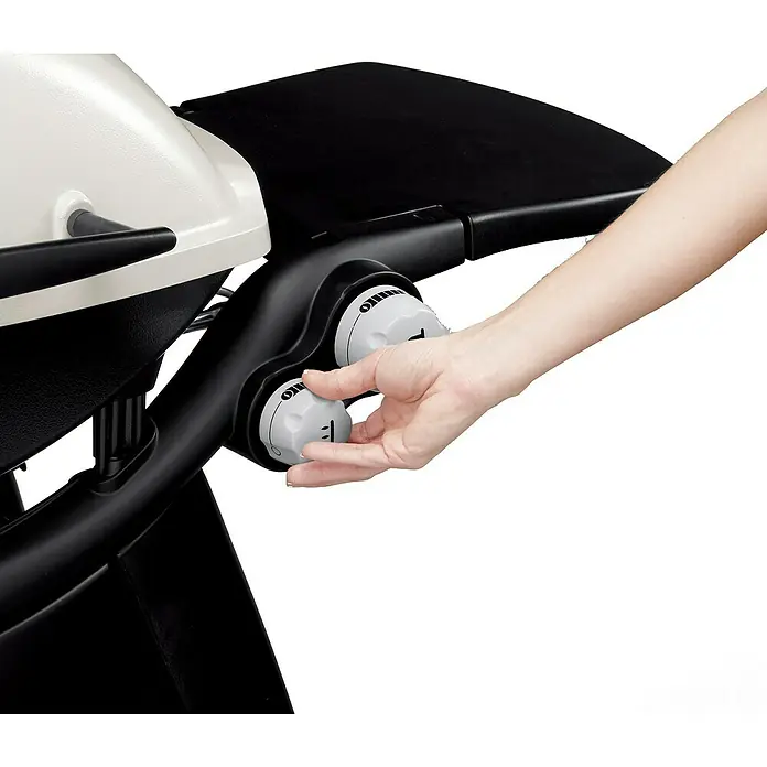 Weber Barbacoa de gas Q3000 - Superficie de la parrilla (An x Pr): 64 x 45 cm, 6,4 kW, Número de quemadores: 2 ud. - Primer plano de una parrilla de exterior con mandos para ajustar el calor, operados por una mano.