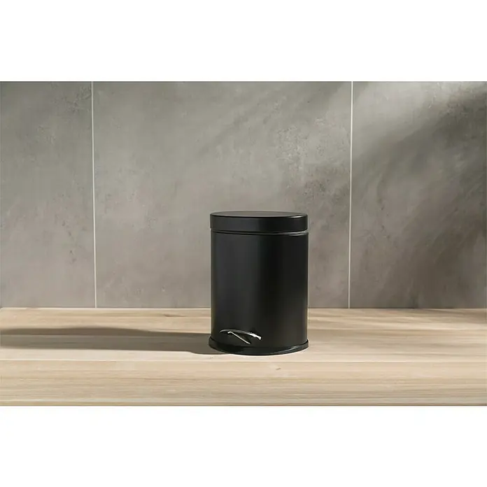 Venus Cubo con pedal Aiko - 3 l, Metal, Negro - Un cubo de basura de pedal cilíndrico negro de metal se encuentra en un piso de madera frente a una pared gris.